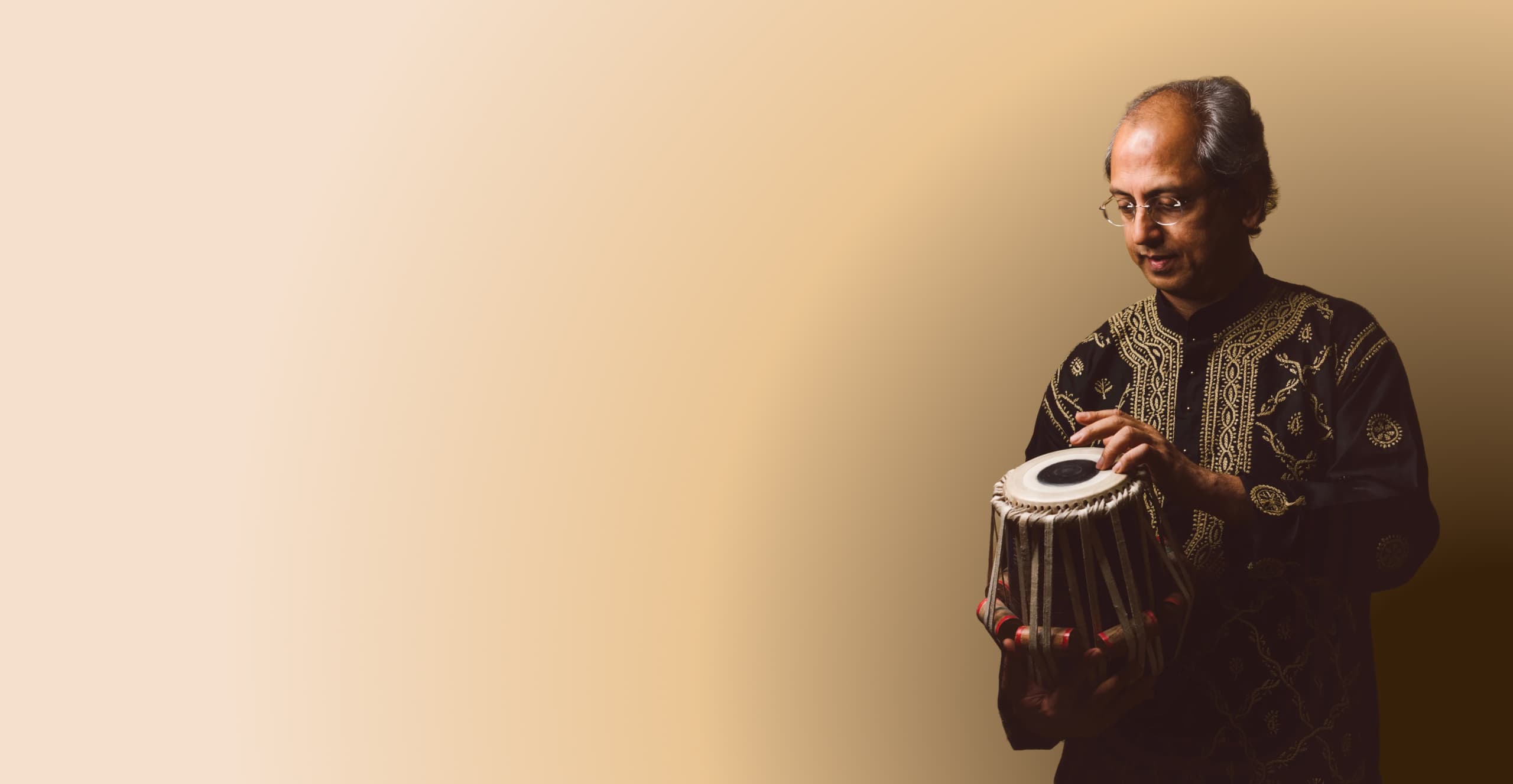 Yogesh Samsi standing holding and playing a tabla.