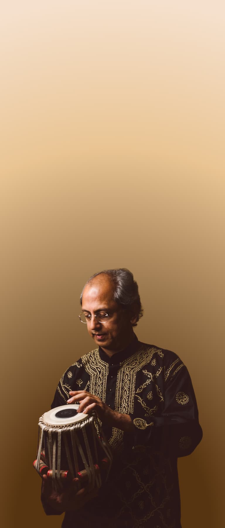 Yogesh Samsi standing holding and playing a tabla.